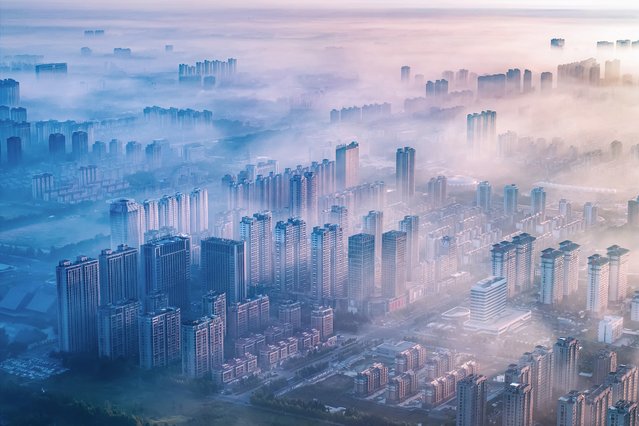 The aerial photo taken on September 25, 2024 shows a general view of sunlight shining through the mist above residential buildings in the morning in Lianyungang, in eastern China's Jiangsu province. (Photo by AFP Photo/China Stringer Network)