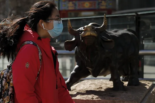 A woman wearing a protective face mask walks by the investment icon bull statue on display outside a bank in Beijing, Tuesday, March 10, 2020. Asian stock markets took a breather from recent steep declines on Tuesday, with several regional benchmarks gaining more than 1% after New York futures reversed on news that President Donald Trump plans to ask Congress for a tax cut and other quick measures to ease the pain of the virus outbreak. (Photo by Andy Wong/AP Photo)