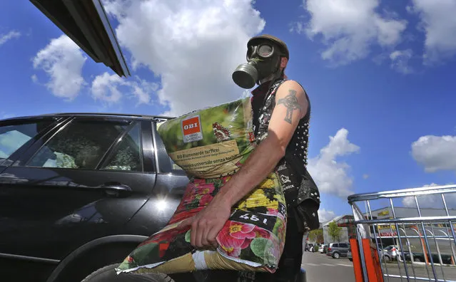 A young man wearing a gas mask loads the potting soil he has bought into his car in front of a hardware store in Kaufbeuren, Germany, Monday, April 27, 2020.  From today face masks are mandatory in parts of Germany for shopping and on public transport due to the coronavirus outbreak. (Photo by Karl-Josef Hildenbrand/dpa via AP Photo)