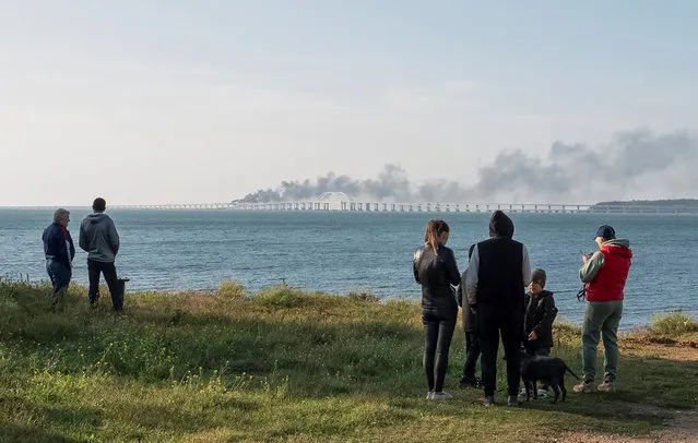 People watch fuel tanks ablaze and damaged sections of the Kerch bridge in the Kerch Strait, Crimea on October 8, 2022. (Photo by Reuters/Stringer)