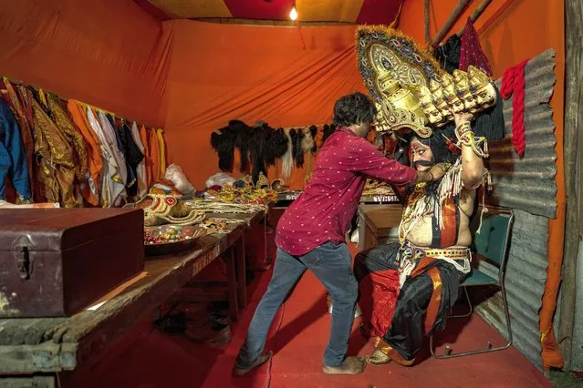 An artist dressed as the demon king Ravana, right, tries to put on an 8-headed crown before a performance of a traditional Ramleela drama to celebrate the festival of Dussehra in New Delhi, India, Tuesday, October 4, 2022. Ramleela is a dramatic folk re-enactment of the life of Hindu lord Rama. After the enactment of the legendary war between Good and Evil, the Ramleela celebrations climax in the Dussehra night festivities where the giant effigies of demon King Ravana, his brother Kumbakaran and son Meghnad are burnt, typically with fireworks. (Photo by Altaf Qadri/AP Photo)