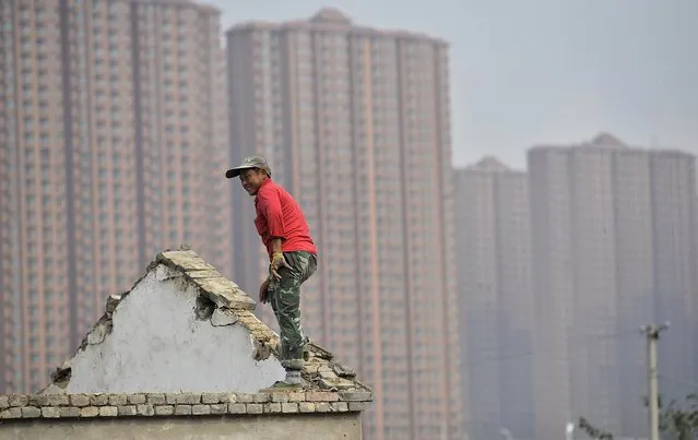 A man stands on the top of a building as farmers' houses are demolished to make space for new property to be built, in front of a residential compound in Hefei, Anhui province, in this October 19, 2013 file photo. (Photo by Reuters/Stringer)