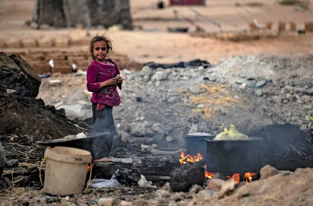 A Syrian girl stands near cooking pots placed on fire amidst the remains of asphalt at the Sahlah al-Banat camp for displaced people in the countryside of Raqa in northern Syria on November 7, 2022. (Photo by Delil Souleiman/AFP Photo)