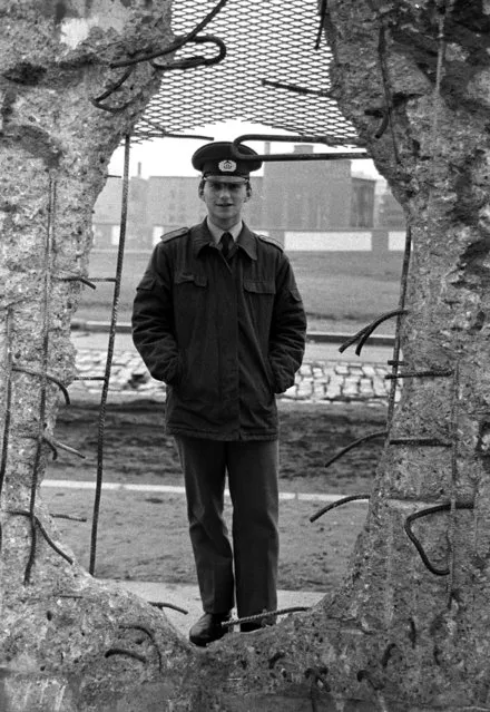 An East German border soldier looks through a large hole into the Berlin Wall after the opening of the East German border was announced, February 8, 1990. (Photo by Reuters)