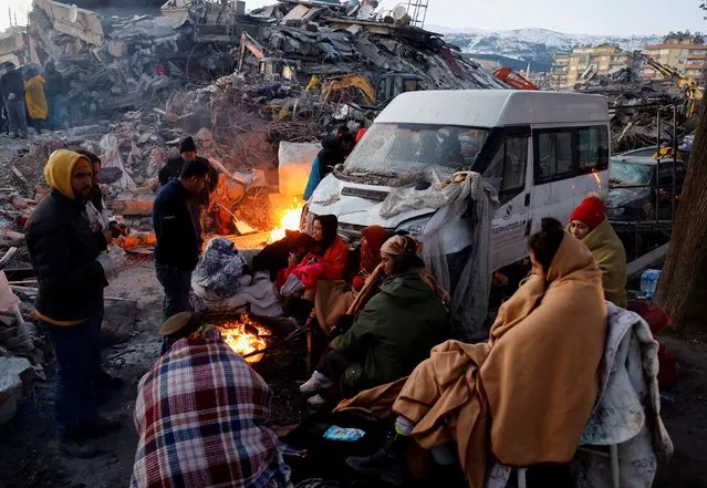 People sit around a fire next to rubble and damages near the site of a collapsed building in the aftermath of an earthquake, in Kahramanmaras, Turkey on February 8, 2023. (Photo by Suhaib Salem/Reuters)