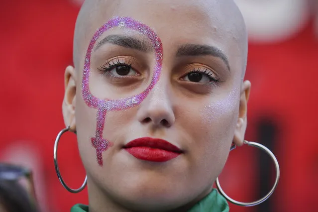 A pro-abortion activist with a Venus symbol painted on her face listens to a speech outside of Congress after the presentation of an abortion bill in Buenos Aires, Argentina, Tuesday, March 6, 2018. Under heavy pressure by women's groups that have taken to the streets in large numbers in recent years, over 70 legislators presented an abortion bill that will be first be discussed in several committees of the lower chamber. (Photo by Victor R. Caivano/AP Photo)