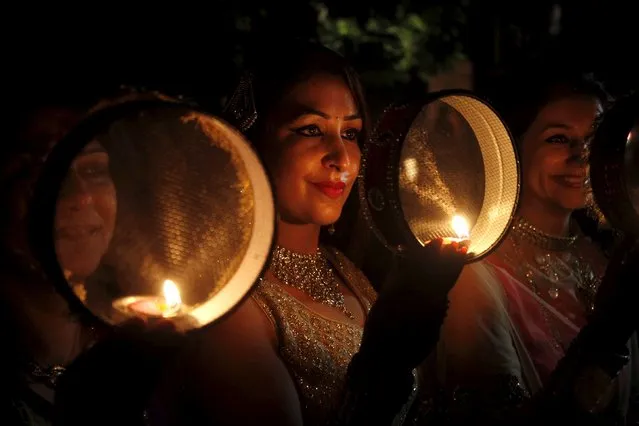 Women look through sieves as they perform a ritual while praying during the Hindu festival of Karva Chauth in Chandigarh, India, October 30, 2015. Married Hindu women observe a one-day fast and offer prayers for the well-being of their husbands during the festival. The fast begins before sunrise and ends after they worship the moon in the evening. (Photo by Ajay Verma/Reuters)