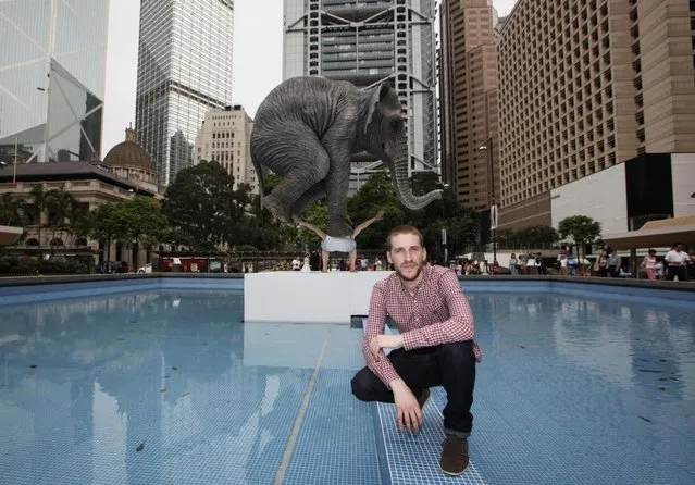 Contemporary French artist Fabien Merelle poses for photographers in front of his creation in five meters high sculpture “Pentateuque” in Central, business district of Hong Kong Tuesday, May 21, 2013. The artwork brings to real life the fantastical and seemingly impossible act of an average man balancing a gigantic elephant. The elephant and the man are modeled on one at the Singapore Zoo and on the artist himself. (AP Photo/Kin Cheung)