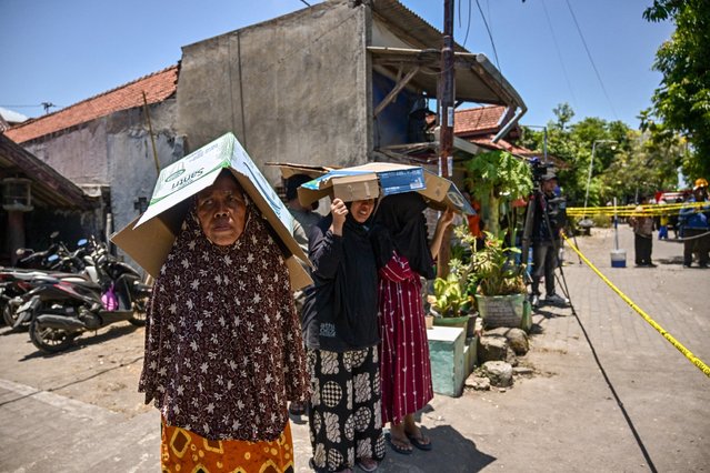 People use cardboard boxes to shelter from the sun as they stand behind a barricade tape as rescuers search for survivors at the Al Khoziny Islamic boarding school in Sidoarjo, East Java province on October 1, 2025, after a multi-storey building at the school collapsed. Rescuers detected “no more signs of life” under the rubble of a collapsed Indonesian school where 59 people remain missing, an official said on October 2, raising fears of a high death toll. (Photo by Juni Kriswanto/AFP Photo)
