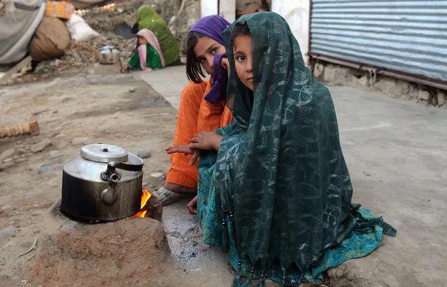 Internally displaced girls warm up by a stove after their family left their village in the Achin district of Afghanistan, due to clashes between the Islamic State group and other insurgent groups, on the outskirts of Jalalabad, east of Kabul, Sunday, November 22, 2015. (Photo by Mohammad Anwar Danishyar/AP Photos)