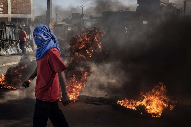 A protester carries stones in front of burning barricades during a demonstration in Antananarivo, Madagascar, on Tuesday, October 7, 2025. Madagascar President Andry Rajoelina said last month that he was dissolving the government following youth-led protests over water and power cuts. At least 22 people have been killed in clashes, and more than 100 have been injured, according to the Reuters news agency. (Photo by Luis Tato/AFP Photo)