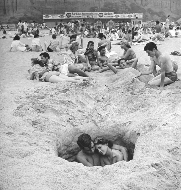 A Young couple cuddles as they sit down in a hole in the sand while others lie around behind them on a hot Independence Day at the beach, Santa Monica, Calif., 1950. (Photo by Ralph Crane/The LIFE Images Collection/Getty Images)
