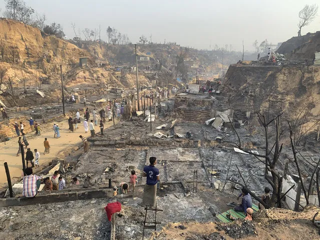 Rohingya refugees look at the remains of Monday's fire at the Rohingya refugee camp in Balukhali, southern Bangladesh, Tuesday, March 23, 2021. The fire destroyed hundreds of shelters and left thousands homeless, officials and witnesses said. (Photo by Shafiqur Rahman/AP Photo)
