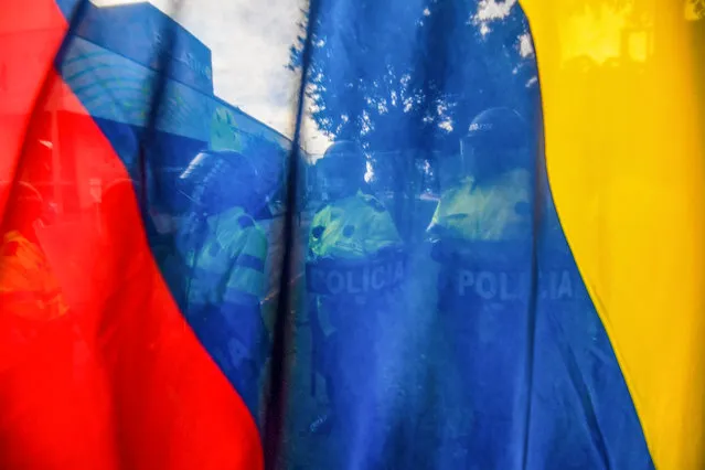Riot police are seen standing guard behind a Colombian flag during a protest against a tax reform bill outside Colombian President Ivan Duque's house in Bogota on May 1, 2021. Thousands of people demonstrated Saturday for the fourth consecutive day in Colombia to demand the withdrawal of a tax reform that, they claim, punishes the middle class in the midst of the pandemic. (Photo by Juan Barreto/AFP Photo)