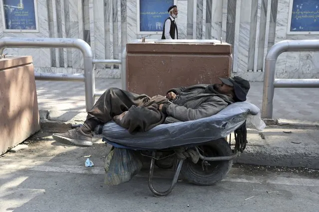 A day laborer sleeps on his hand cart while waiting for customers on the first day of the Muslim holy fasting month of Ramadan, in Kabul, Afghanistan, Tuesday, April 13, 2021. Ramadan is marked by daily fasting from dawn to sunset, ending with the Islamic holiday of Eid al-Fitr. (Photo by Rahmat Gul/AP Photo)