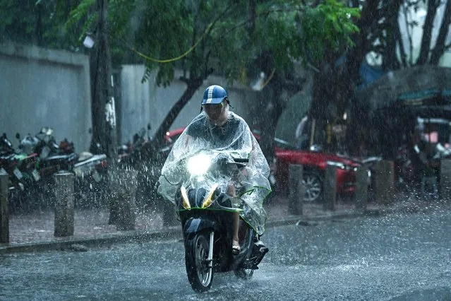 A man rides a motorbike in the rain in Hanoi on August 11, 2023. (Photo by Nhac Nguyen/AFP Photo)