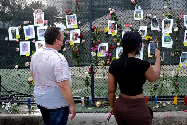 People look at flowers and pictures of missing people hanging on a fence at the memorial for victims of a partially collapsed residential building as the emergency crews continue search and rescue operations for survivors, in Surfside, near Miami Beach, Florida, U.S. June 26, 2021. (Photo by Marco Bello/Reuters)