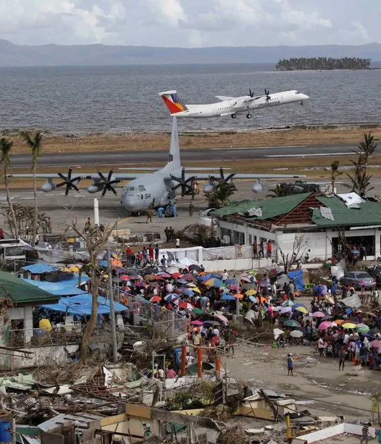 A Philippine Airlines passenger plane takes off as typhoon survivors in lines take their chance to board U.S. military transport planes from the damaged airport in Tacloban city, Leyte province in central Philippines, Wednesday November 13, 2013. (Photo by Bullit Marquez/AP Photo)
