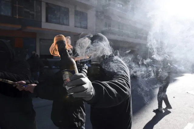 A hooded youth prepares to throw a petrol bomb at riot police in the northern Greek city of Thessaloniki, on Thursday, December 6, 2018 during a rally commemorating the killing of a 15-year old student back in 2008. School and university students marched in various towns of the country to mark the tenth anniversary of a fatal police shooting of a teenager in Athens that sparked the worst rioting Greece had seen in decades. (Photo by Giannis Papanikos/AP Photo)