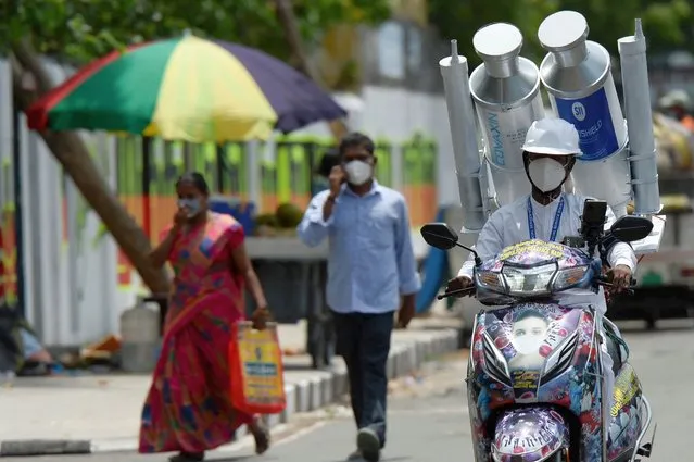 A volunteer rides along a road with a mock Covishield and Covaxin vaccine vials on the back of his scooter during a Covid-19 coronavirus vaccination awareness campaign, in Chennai, India on August 2, 2021. (Photo by Arun Sankar/AFP Photo)