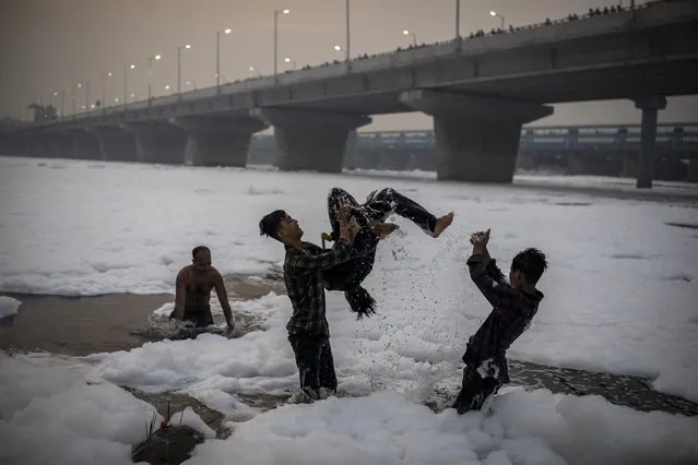 Young Hindu devotees play in Yamuna river, covered by chemical foam caused due to industrial and domestic pollution, during Chhath Puja festival in New Delhi, India, Wednesday, November 10, 2021. A vast stretch of one of India's most sacred rivers, the Yamuna, is covered with toxic foam, caused partly by high pollutants discharged from industries ringing the capital New Delhi. Still, hundreds of Hindu devotees Wednesday stood knee-deep in its frothy, toxic waters, sometimes even immersing themselves in the river for a holy dip, to mark the festival of Chhath Puja. (Photo by Altaf Qadri/AP Photo)