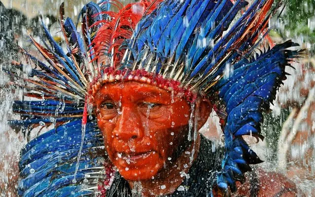An Indigenous man stands under a water fountain outside a government building in Brasilia, on April 26, 2019, during the last day of a protest camp. Approximately 4,000 indigenous people from different tribes are taking part in protests during the Indigenous National Mobilization (MNI) week, a mobilization which seeks to tackle territorial rights' negotiations with the government. (Photo by Carl De Souza/AFP Photo)