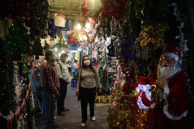 People walk in an alley hanging with decorations for sale ahead of Christmas in Kolkata, India, Wednesday, December 8, 2021. Although Christians comprise only two percent of the population Christmas is a national holiday and is observed across the country as an occasion to celebrate. (Photo by Bikas Das/AP Photo)