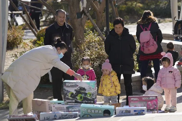 A vendor shows toys to young children on the street of Beijing, China, Tuesday, Dec. 7, 2021. Chinese leaders on Friday, December 10, 2021 promised tax cuts and support for entrepreneurs next year to shore up slumping economic growth after a campaign to rein in surging corporate debt caused bankruptcies and defaults among real estate developers. (Photo by Ng Han Guan/AP Photo)