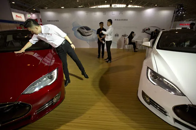 An employee cleans the hood of a Tesla Model S electric car on display at the Beijing International Automotive Exhibition in Beijing, Monday, April 25, 2016. (Photo by Mark Schiefelbein/AP Photo)