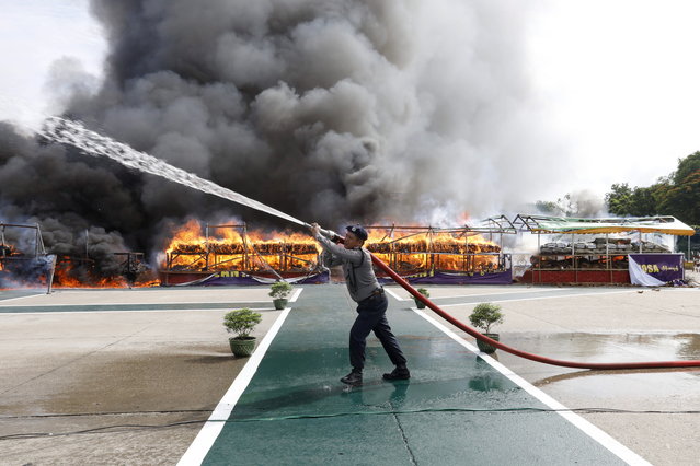 A police officer uses a water cannon on a temporary tent to reduce heat near a pile of illegal drugs burning during a “Destruction Ceremony of Seized Narcotic Drugs”, held to mark the International Day against Drug Abuse, in Yangon, Myanmar, 26 June 2019. Myanmar authorities destroyed an assortment of drugs worth around 301.16 million US dollar in Yangon, Mandalay and Taunggyi. (Photo by Nyein Chan Naing/EPA/EFE)