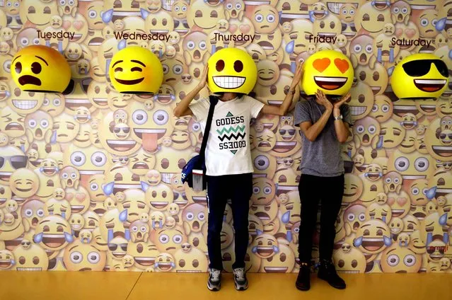 In this Wednesday, May 18, 2016, 2016, passers-by pose for photos with emoji masks fixed onto a wall at a shopping mall in Guangzhou in south China's Guangdong province. Emoji icons are popularly used for social media communication as they transcend cultural barriers and are fun to use. (Photo by Chinatopix via AP Photo)