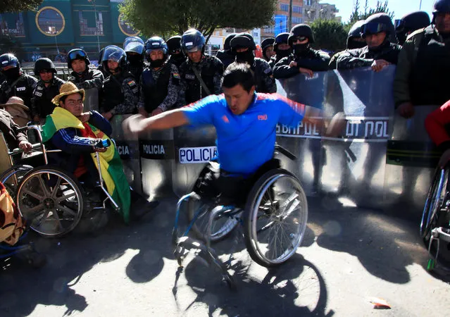 A demonstrator with a physical disability dances in his wheelchair in front of riot policemen during a protest calling on the government to provide a monthly subsidy for the physically disabled rather than an annual one, in El Alto, Bolivia, May 30, 2016. (Photo by David Mercado/Reuters)