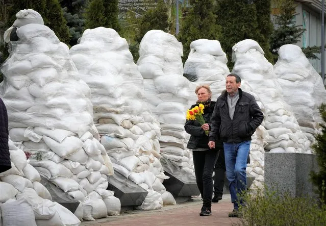 People pay respect to the Chernobyl firefighters at a memorial in capital Kyiv, Ukraine, Tuesday, April 26, 2022. At left, firefighter sculptures are covered with bags to protect against the Russian shelling. April 26 marks the 36th anniversary of the Chernobyl nuclear disaster. A reactor at the Chernobyl nuclear power plant exploded on April 26, 1986, leading to an explosion and the subsequent fire spewed a radioactive plume over much of northern Europe. (Photo by Efrem Lukatsky/AP Photo)