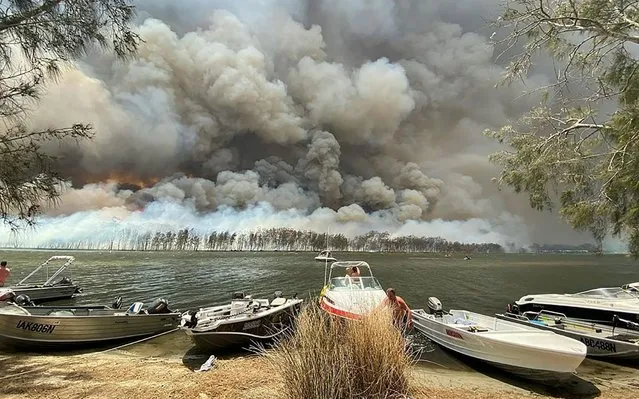 Boats are pulled ashore as smoke and wildfires rage behind Lake Conjola, Australia, Thursday, January 2, 2020. Thousands of tourists fled Australia's wildfire-ravaged eastern coast Thursday ahead of worsening conditions as the military started to evacuate people trapped on the shore further south. (Photo by Robert Oerlemans via AP Photo)
