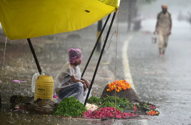 An Indian boy covers himself with a plastic sheet as he waits for customers at a flower stall during heavy rain in Allahabad on July 11, 2017. (Photo by Sanjay Kanojia/AFP Photo)