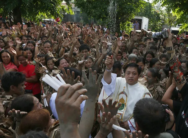 Fr. Elmer Villamayor blesses villagers, donning capes mostly of dried banana leaves and covered in mud, following a mass in a bizarre annual ritual to venerate their patron saint, John the Baptist, Friday, June 24, 2016 at Bibiclat, Aliaga township, Nueva Ecija province in northern Philippines. (Photo by Bullit Marquez/AP Photo)