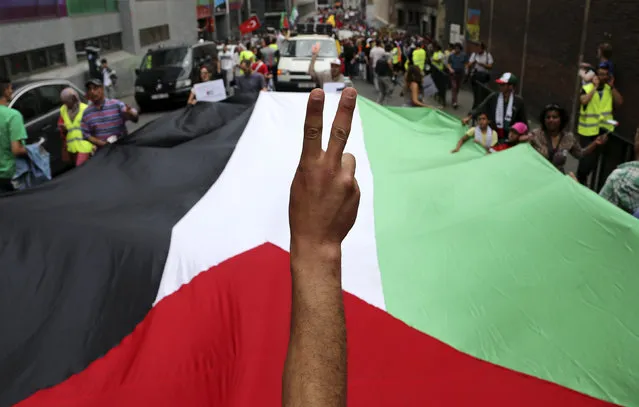 A demonstrator flashes a victory sign in front of a Palestinian flag during a protest against Israel's military action in Gaza, in central Brussels July 19, 2014. (Photo by Francois Lenoir/Reuters)