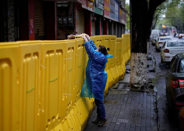 A woman wearing a face mask passes eggs above the barriers, which have been built to block buildings from a street in Wuhan, Hubei province, the epicenter of China's coronavirus disease (COVID-19) outbreak, March 29, 2020. (Photo by Aly Song/Reuters)