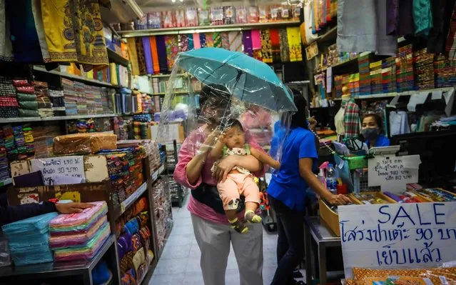 A woman carries a baby under an umbrella with a plastic covering as a preventive measure against the spread of the COVID-19 novel coronavirus at a market in Bangkok on March 24, 2020. Thailand is set to declare a state of emergency to slow the spread of a virus which has killed four in the kingdom, its premier said March 24. (Photo by Vivek Prakash/AFP Photo)
