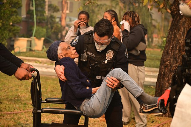 Police officers remove an eldery resident from her home during the Eaton Fire in Altadena, California, on January 8, 2025. Rampaging wildfires around Los Angeles have killed at least two people, officials said January 8 as terrifying blazes leveled whole streets, torching cars and houses in minutes. More than 1,000 buildings have burned in multiple wildfires that have erupted around America's second biggest city, forcing tens of thousands of people from their homes. (Photo by Robyn Beck/AFP Photo)