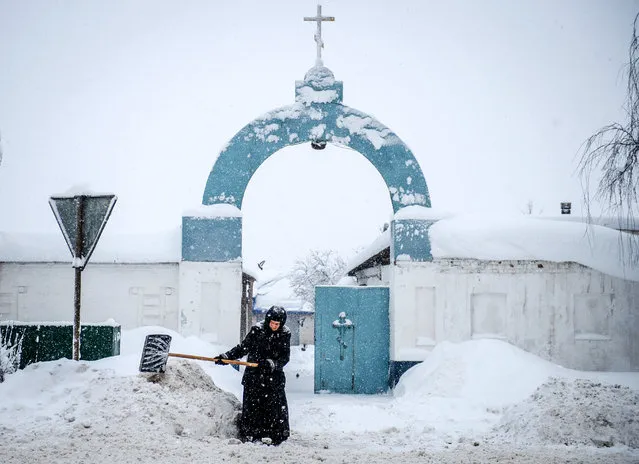 A nun removes snow during a snowfall in front of the gate of the Bogoslovsky nunnery in the village of Bogoslovo in Vladimirsky region some 190 km outside Moscow on February 4, 2018. (Photo by Konstantin Chalabov/AFP Photo)