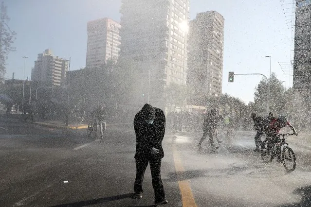 People are sprayed by a water cannon as they attend a protest against Chile's government, in Santiago, Chile on October 2, 2020. (Photo by Ivan Alvarado/Reuters)