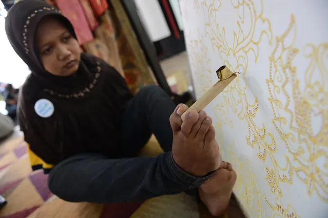 Ayu, a 22 year old handicapped Indonesian applies wax with her foot to create a batik design with a canting or wax pen on a cotton fabric during a demonstration in Jakarta, on March 26, 2013. Ayu born with a congenital handicap overcame her disability when she studied in regular public school and at the age of 17 learnt the art of batik making. Ayu finishes wax patterns on a cloth in about one week. Ayu and her family lives in Solo city, a key batik fabric producing area in central Java island. (Photo by Romeo Gacad)
