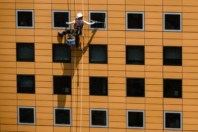 A window cleaner uses a squeegee while rappelling down a commercial building in Seoul on June 23, 2025. (Photo by Anthony Wallace/AFP Photo)