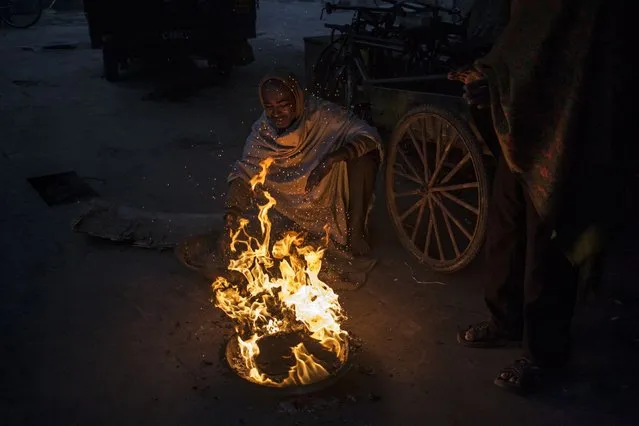 Indian men stay warm near a fire in New Delhi, India, Monday, December 22, 2014. Cold wave conditions intensified across northern India as temperatures dipped along with thick blankets of fog cutting out sunlight for long hours. (Photo by Tsering Topgyal/AP Photo)