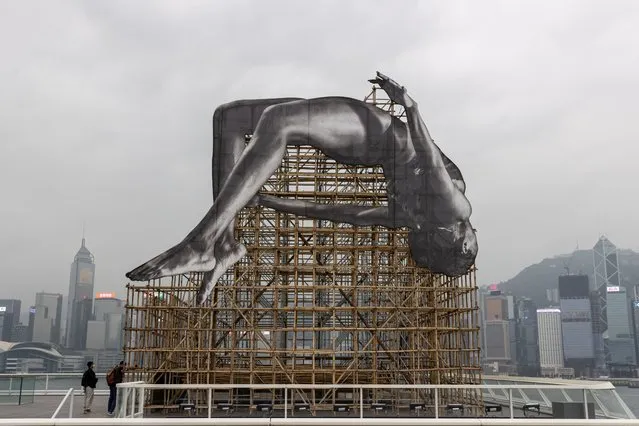 Visitors take a look at the art piece “GIANTS: Rising Up” at Harbour City in Hong Kong China, 13 March 2023. The 12-meter-high and 12-meter-wide installation by French artist JR depicts a larger-than-life high jumper floating in mid-air adjacent to Victoria Harbour. It will be displayed until 23 April. (Photo by Jerome Favre/EPA)
