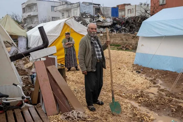 A man with a shovel stands in his slippers in the mud close to tents set up for displaced people  following a massive earthquake last month, in Adiyaman, southeastern Turkey on March 25, 2023. (Photo by Bulent Kilic/AFP Photo)