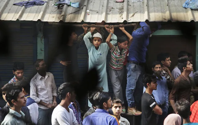 Locals crowd outside a residential building used as a garment factory, which was gutted in a fire in the outskirts of New Delhi, India, Friday, November 11, 2016. The fire, that broke out at the garment factory basement, trapped and killed more than a dozen workers as they slept in the building. (Photo by Altaf Qadri/AP Photo)