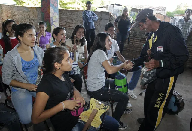 Trash recycler and craftsman Nicolas Gomez (R) greets students of the Orchestra of Recycled Instruments of Cateura, for which Gomez makes all their instruments, in Cateura, near Asuncion, May 9, 2013. The orchestra is the brainchild of its conductor Favio Chavez, who wanted to help the children of garbage pickers at the local landfill, and the instruments are made from salvaged materials by craftsman Gomez. (Photo by Jorge Adorno/Reuters)