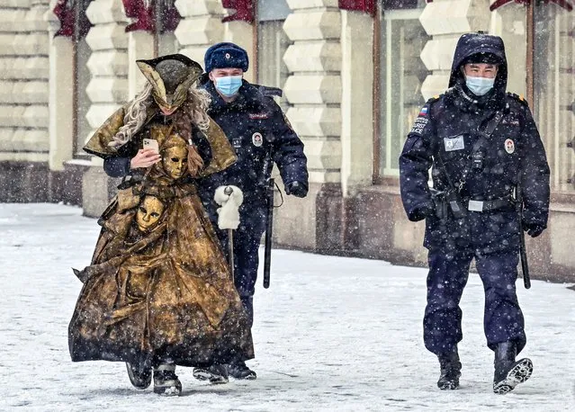 Two police officers and a woman in a carnival costume walk in the snowfall, in Moscow, on March 13, 2021. (Photo by Yuri Kadobnov/AFP Photo)
